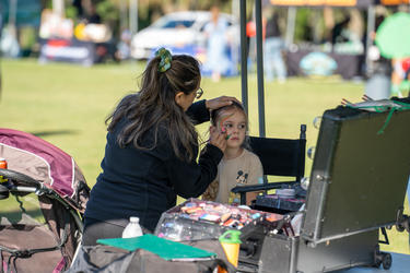 a woman painting the face of a child under a tent with paint and brushes on a table